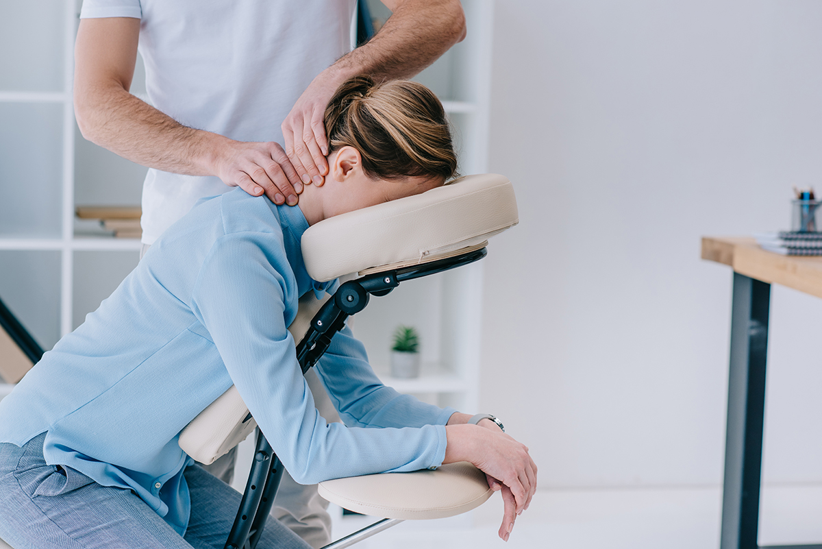 Woman in a blue top sitting on a massage chair face down, getting a neck massage